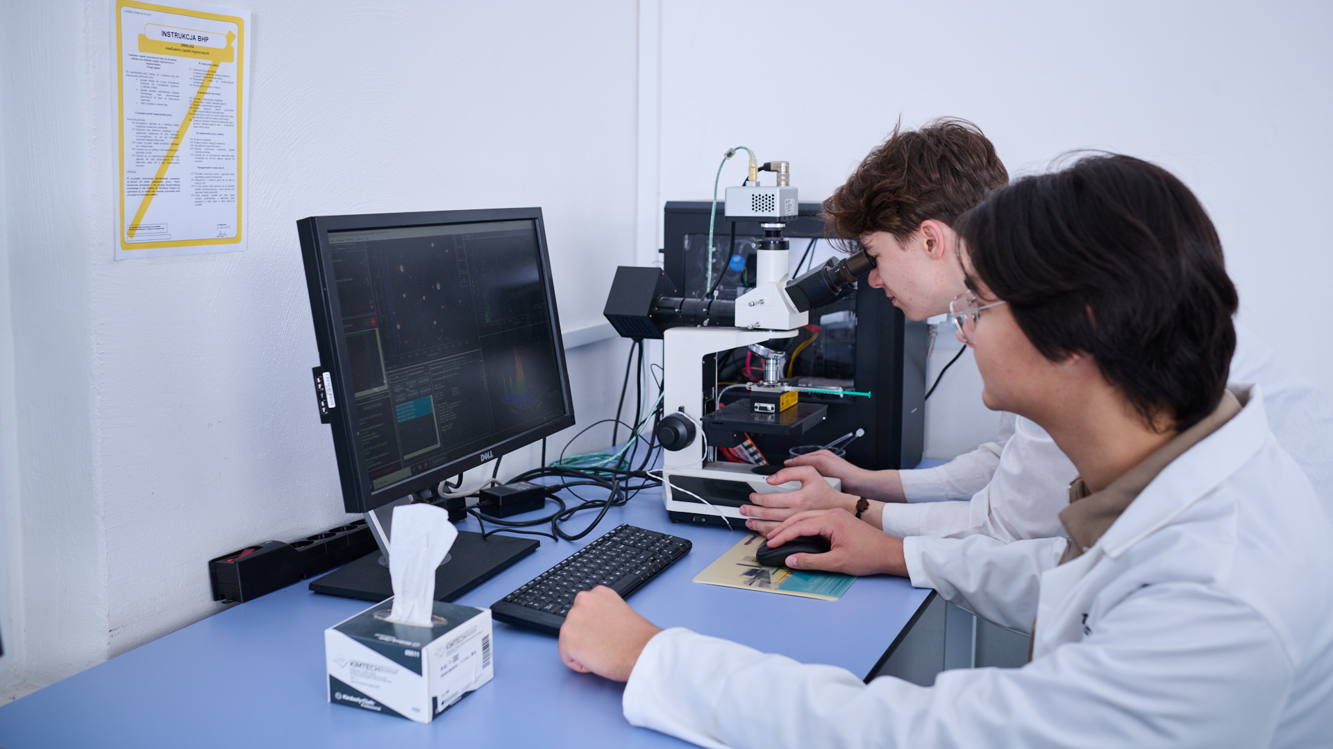 Na zdjęciu dwie osoby siedzące przy komputerze i mikroskopie