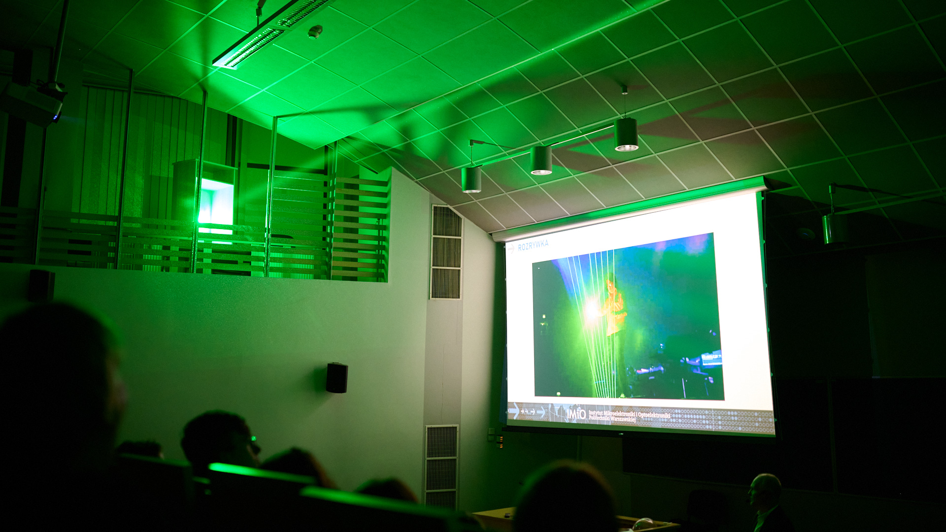 Na zdjęciu zielone światło laserowe w sali wypełnionej ludźmi