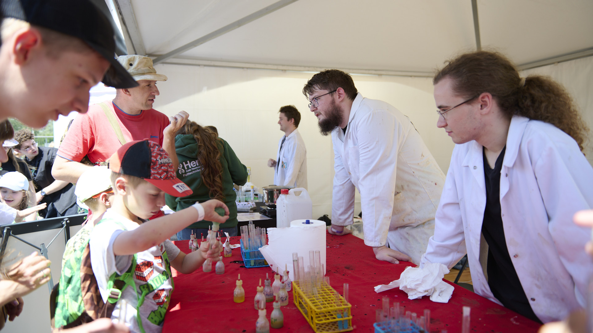 Na zdjęciu grupa ludzi przy stanowisku z eksperymentami chemicznymi