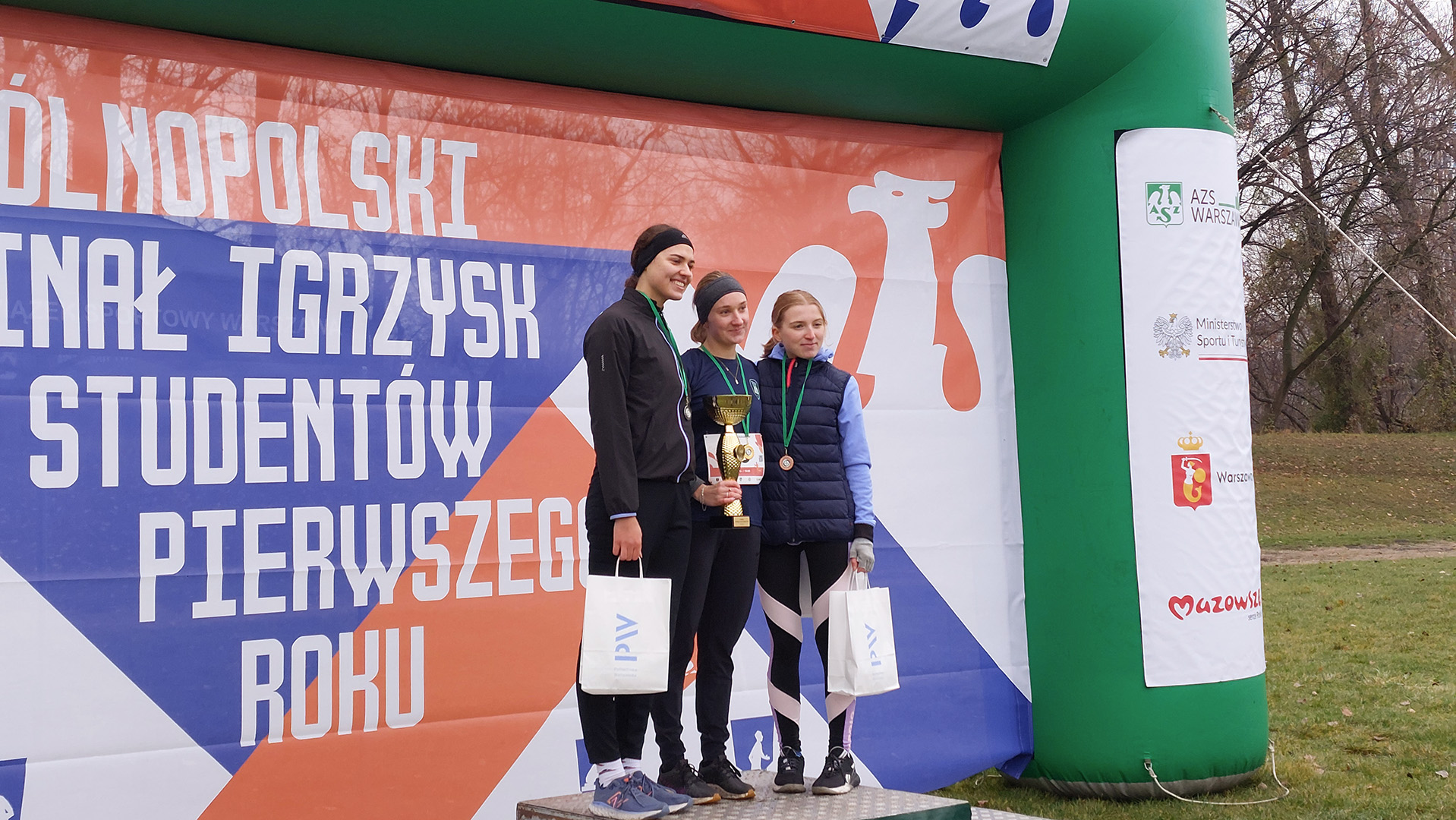 Trzy studentki stoją na podium z nagrodami