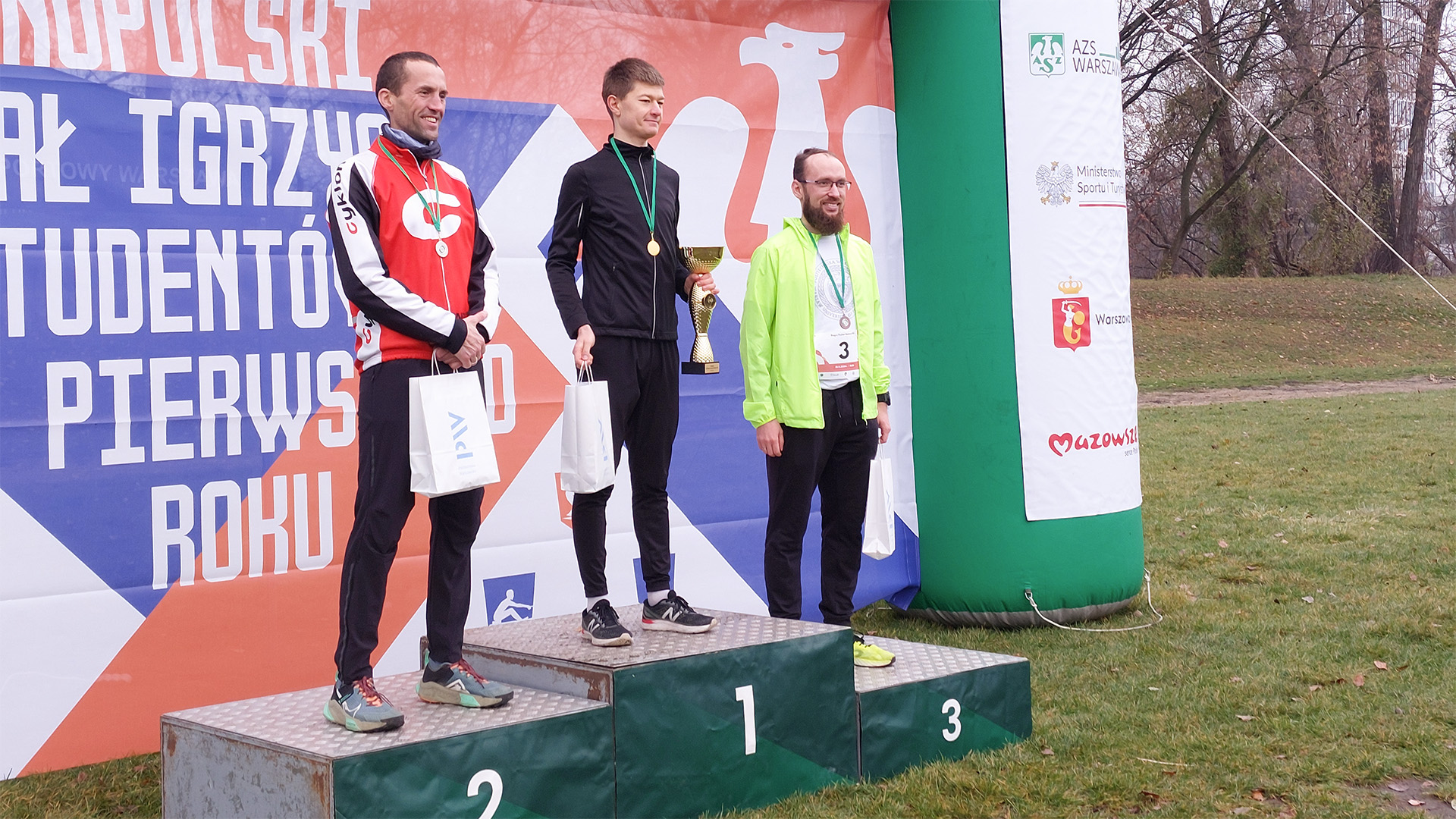 Trzej mężczyźni stoją na podium z nagrodami