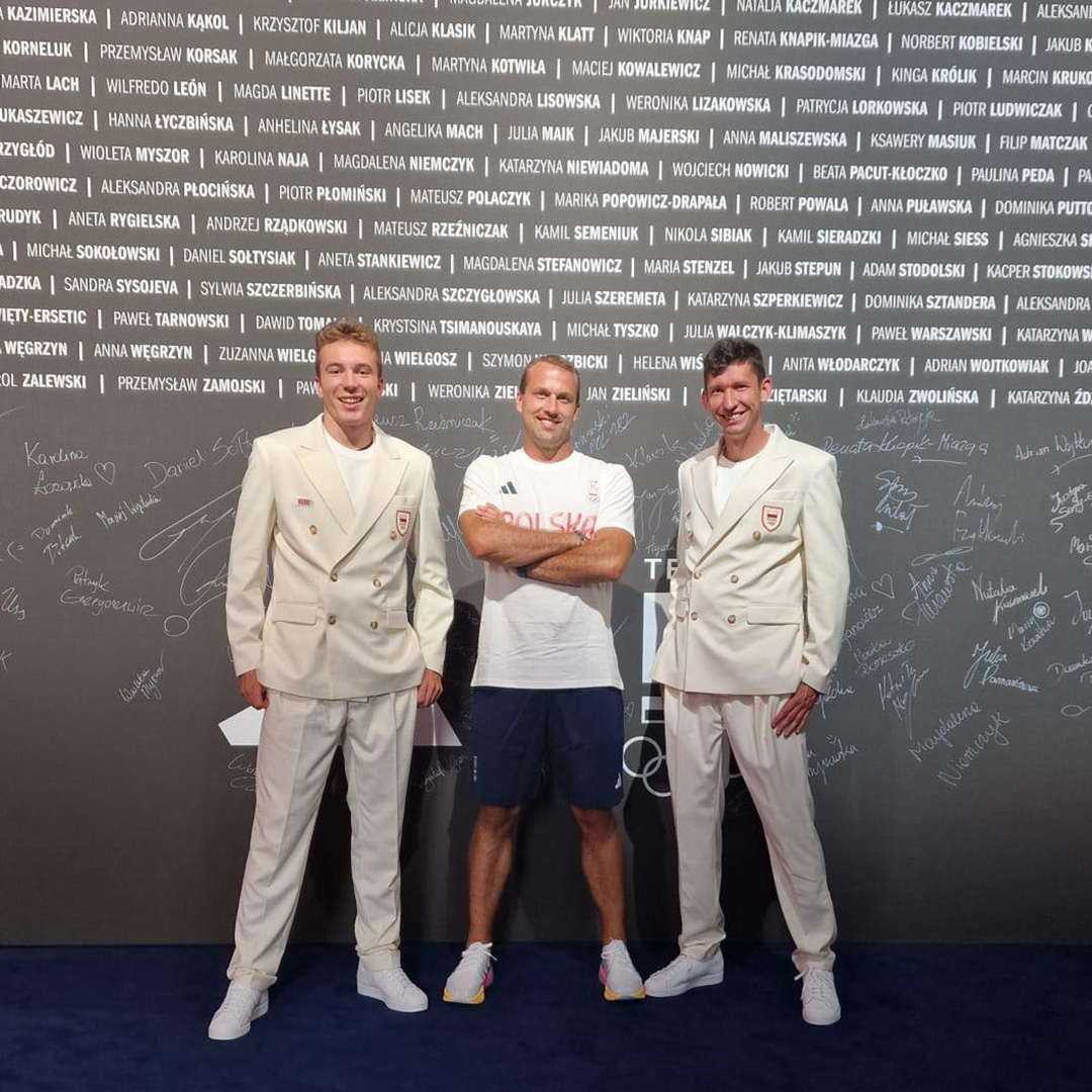 Na zdjęciu trzech mężczyzn stojących na tle ściany z nazwiskami polskich olimpijczyków 2024