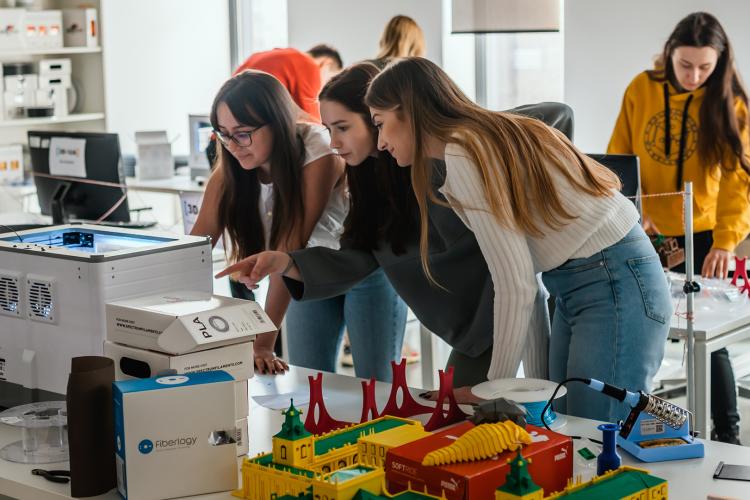 Na zdjęciu trzy studentki pochylone nad drukarką 3D