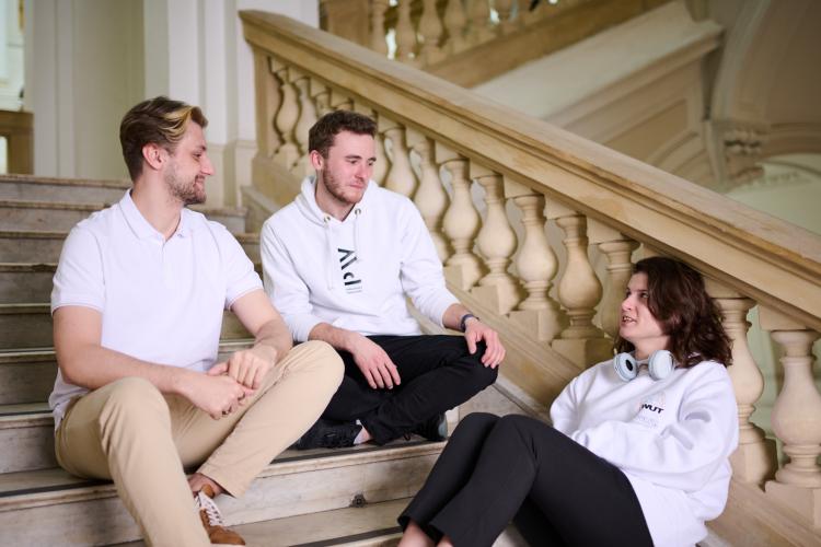 Na zdjęciu dwóch studentów i studentka siedzą na schodach w Gmachu Głównym PW
