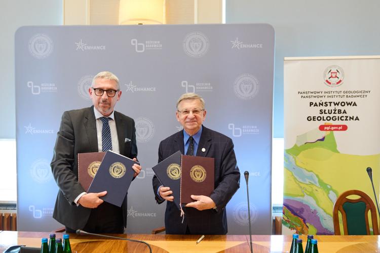 Za zdjęciu prof. Mariusz Malinowski oraz prof. Krzysztof Szmałek trzymający podpisane umowy, stojący na tle ścianki i roll-upu