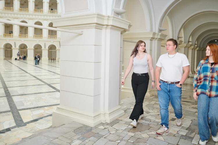 Na zdjęciu cztery osoby: dwie studentki i jeden student idą korytarzem w Gmachu Głównym PW