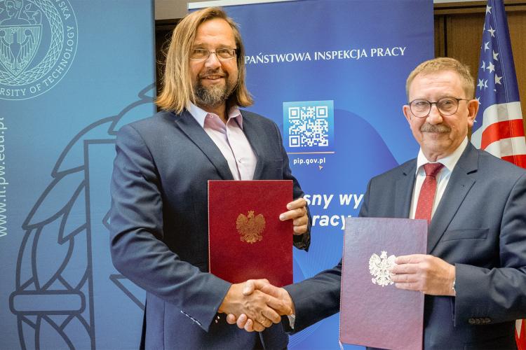 Na zdjęciu Marcin Stanecki – Główny Inspektor Pracy oraz prof. dr hab. inż. Andrzej Garbacz – Dziekan Wydziału Inżynierii Lądowej PW stoją na tle ścianek i ściskają sobie dłonie