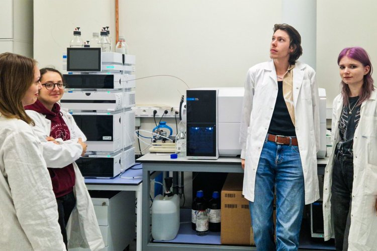 Na zdjęciu pięcioro studentów ubranych w białe fartuchy laboratoryjne w laboratorium chemicznym