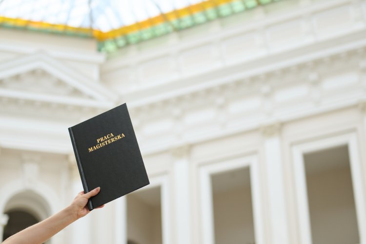 Na zdjęciu widać trzymaną pracę magisterską na tle wnętrza Gmachu Głównego PW