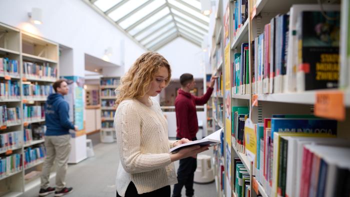 Studenci szukający książek w bibliotece