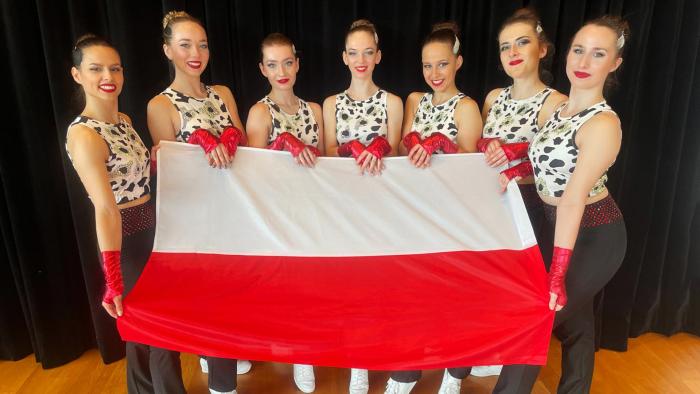 Na zdjęciu siedem zawodniczek z sekcji aerobiku sportowego. Stoją, trzymając przed sobą flagę Polski