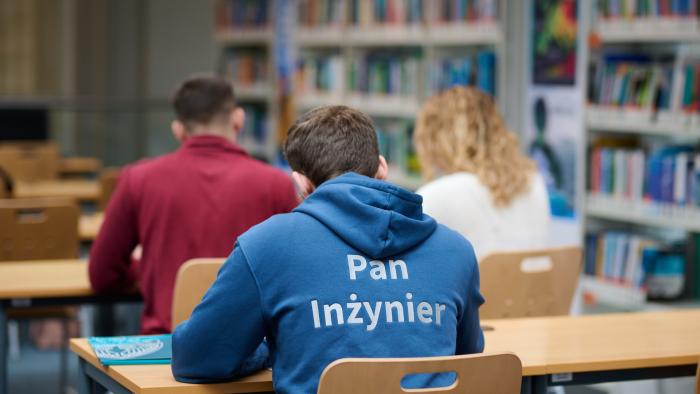 Na zdjęciu trzy osoby (widziane od tyłu) siedzące przy stolikach w Bibliotece Głównej PW