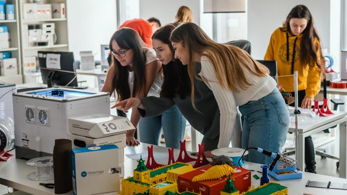 Na zdjęciu trzy studentki pochylone nad drukarką 3D