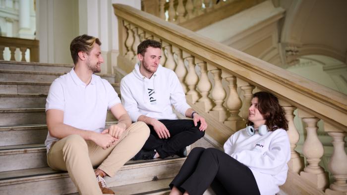 Na zdjęciu dwóch studentów i studentka siedzą na schodach w Gmachu Głównym PW