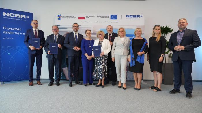 Na zdjęciu grupa stojących osób: przedstawiciele Politechniki Warszawskiej, Sopockiej Akademii Nauk Stosowanych, Zachodniopomorskiego Uniwersytetu Technologicznego w Szczecinie wraz z Ministrem Nauki Marcinem Kulaskiem i Dyrektorem NCBR prof. Jerzym Małachowskim 