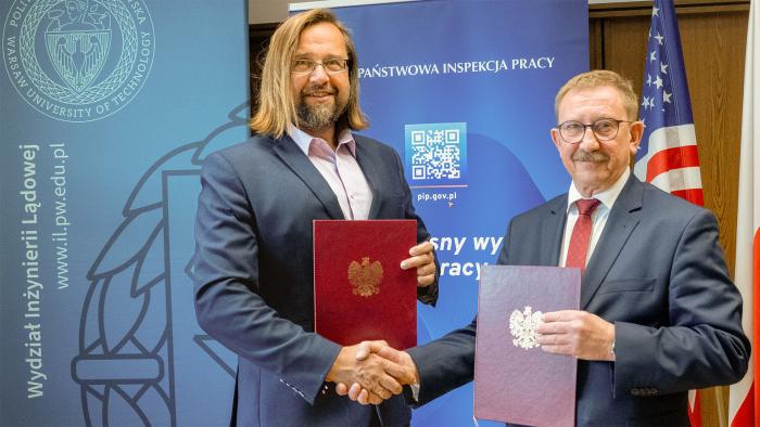 Na zdjęciu Marcin Stanecki – Główny Inspektor Pracy oraz prof. dr hab. inż. Andrzej Garbacz – Dziekan Wydziału Inżynierii Lądowej PW stoją na tle ścianek i ściskają sobie dłonie