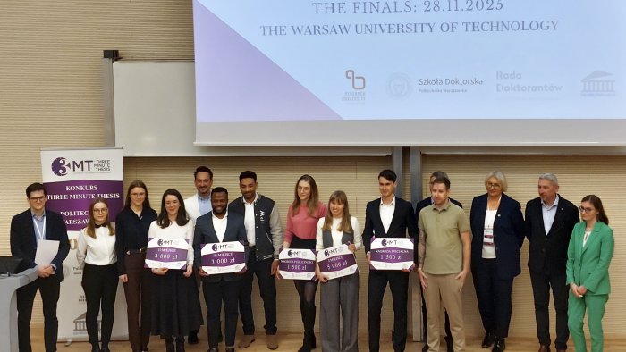 Zdjęcie przedstawia laureatów i jurorów konkursu Three Minute Thesis na Politechnice Warszawskiej stojących razem na scenie. Laureaci trzymają tablice z przyznanymi nagrodami.