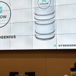 Zdjęcie pokazujące ekran z prezentacją o rozwiązaniu Hyflow oraz zespołu lidera przy mównicy