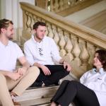 Na zdjęciu dwóch studentów i studentka siedzą na schodach w Gmachu Głównym PW