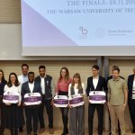 Zdjęcie przedstawia laureatów i jurorów konkursu Three Minute Thesis na Politechnice Warszawskiej stojących razem na scenie. Laureaci trzymają tablice z przyznanymi nagrodami.